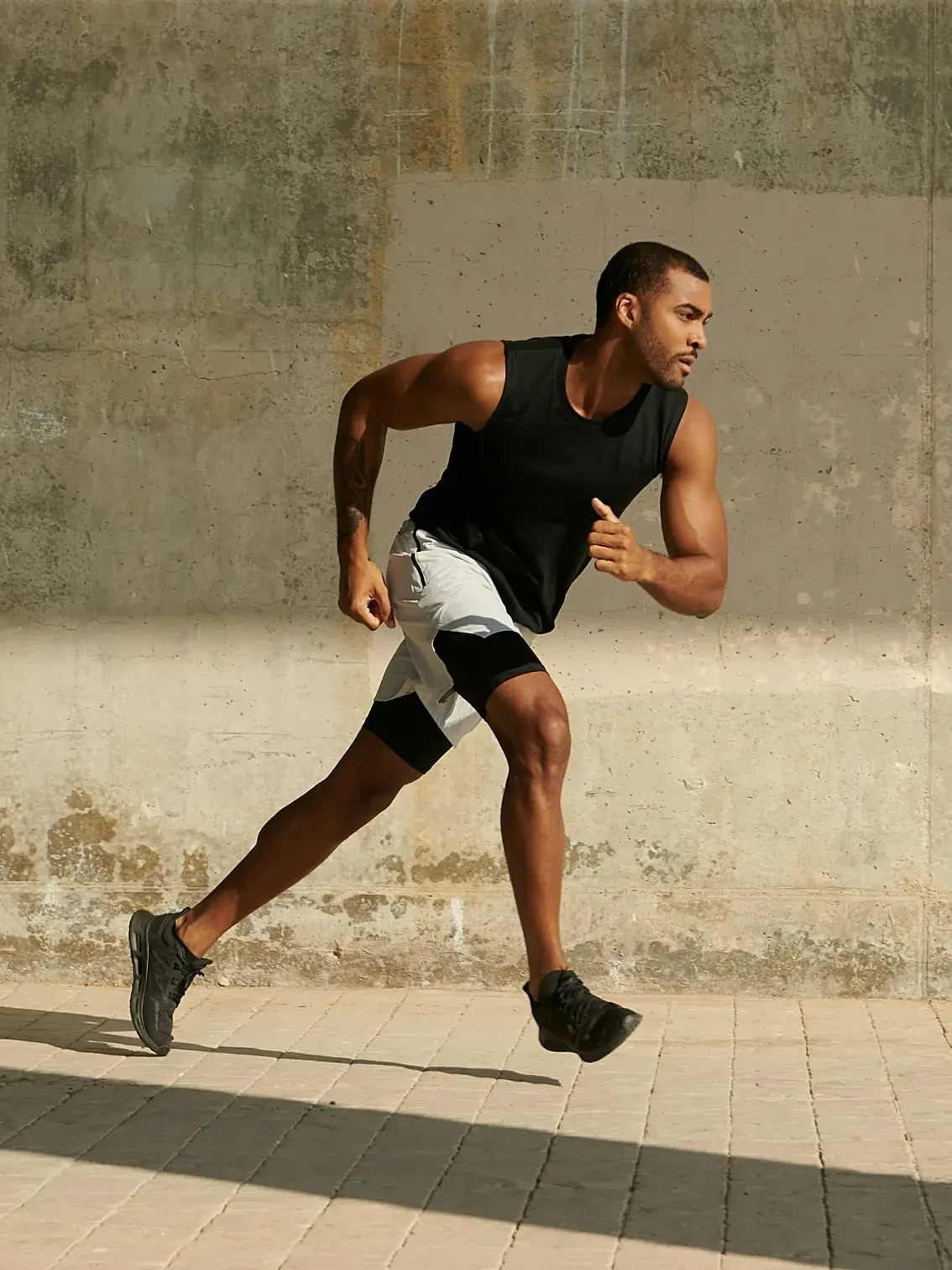 A man sprinting along a sunlit concrete wall